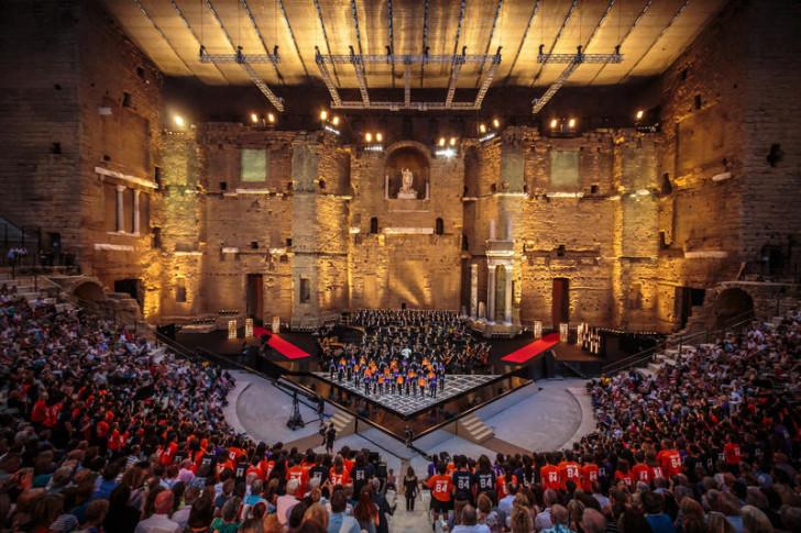 Photo prise depuis les gradins à la nuit tombée. Sur la scène au premier plan, l'orchestre et à l'arrière, on aperçoit le chœur